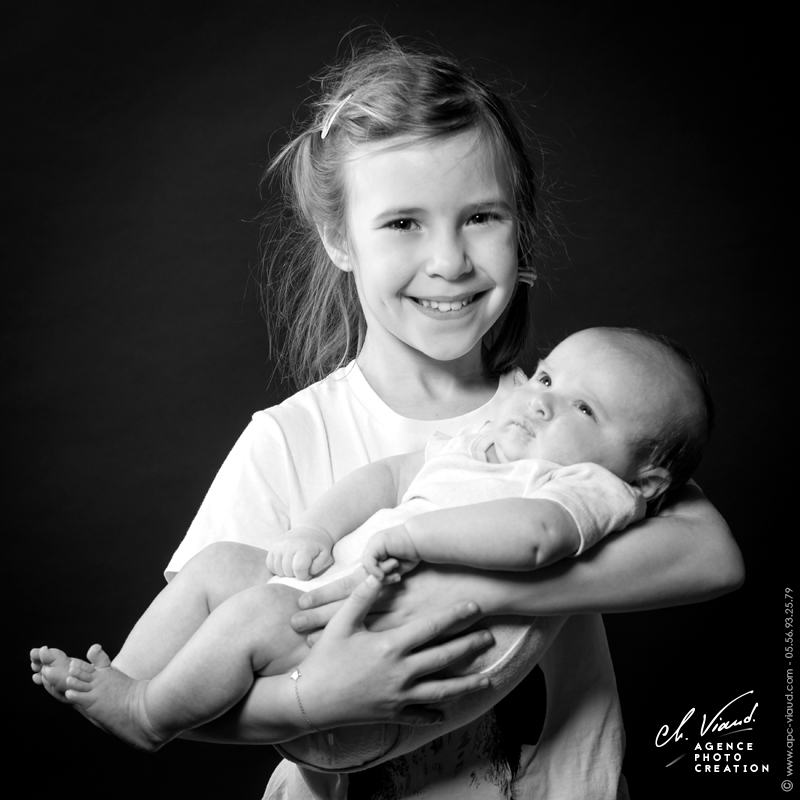 Joli portrait studio d'une petite fille avec son nouveau petit frère dans les bras