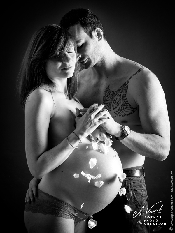 Portrait studio d'une couple pendant la grossesse avec des pétales qui tombent sur le ventre