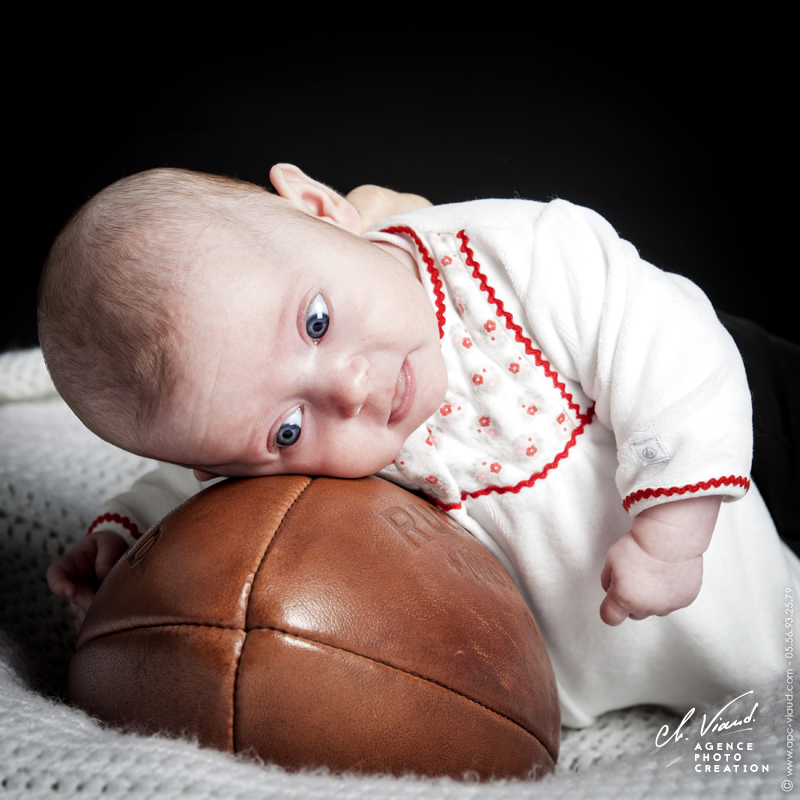 Portrait studio d'un bébé couché sur un ballon de rugby