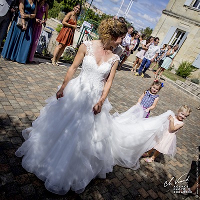 Reportage mariage - Photo de la mariée devant la mairie avec des petites filles lui tenant sa robe